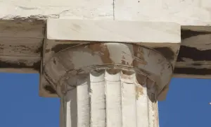Kamienna kolumna w stylu porządek dorycki, z widocznymi żłobieniami i ozdobnym kapitelem, na tle błękitnego nieba.