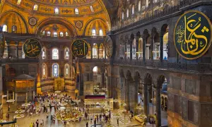 Wnętrze Hagia Sophia z widokiem na kopułę, kaligrafię i turystów. Plan budowli ukazuje jej monumentalność.