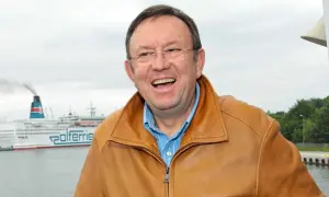 Uśmiechnięty Zbigniew Buczkowski w brązowej kurtce, na tle promu Polferries. Jego filmy, seriale i programy to klasyka polskiej rozrywki.