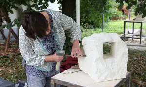 Kobieta rzeźbi w kamieniu, używając dłuta i młotka.