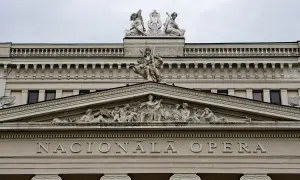 Elegancka fasada budynku opery w stylu neoklasycyzmu, ozdobiona rzeźbami i napisem "NACIONĀLĀ OPERA".