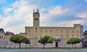 Budynek z wieżą i zegarem, otoczony drzewami. Czy to kordegarda? Co to za miejsce?