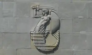 Warszawska Syrenka w płaskorzeźbie na kamiennej ścianie, trzymająca miecz i tarczę.