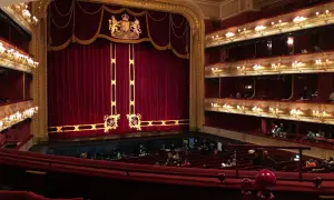 Wnętrze teatru z czerwonymi aksamitnymi zasłonami i lożami. Słychać śpiewaka operowego, który przygotowuje się do występu.