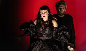 Dramatyczna scena z opery Karola Szymanowskiego. Kobieta w czarnej sukni i mężczyzna z wyrazem przerażenia na twarzy.