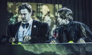 Dwóch mężczyzn przy stole, jeden w czarnym aksamicie, drugi w koronkowej szacie. Może to Hamlet i Ofelia?