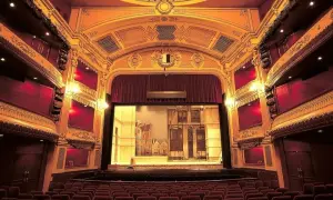 Widok na salę teatralną z rzędami czerwonych foteli i sceną z dekoracjami.
