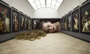 Kobieta leżąca na podłodze galerii sztuki, otoczona obrazami.
