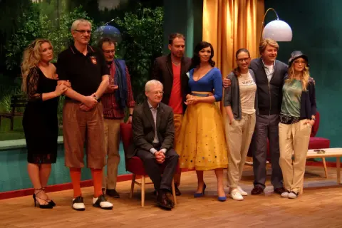 Miłość w Saybrook: obsada w komplecie, od lewej: blondynka w czarnej sukience, mężczyzna w czarnej koszulce polo, mężczyzna w kratę, siedzący mężczyzna w garniturze, kobieta w żółtej sukience, kobieta w szarej bluzie, mężczyzna w granatowej kurtce, kob...