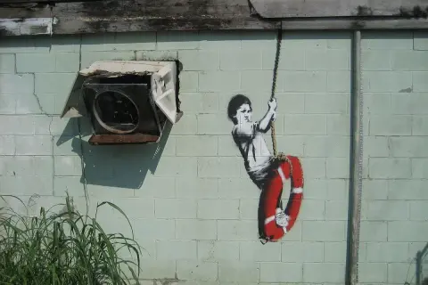 Dziecko na huśtawce z kołem ratunkowym, dzieło Banksy'ego. Kto to? Tajemniczy artysta uliczny.