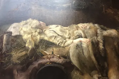 Młoda kobieta o blond włosach, Ellenai, śpi otulona futrem. Obok niej leży krzyż i książka.