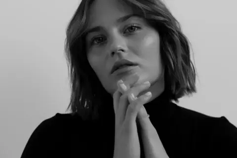 Katarzyna Sawczuk w czarnym golfie, z dłońmi złożonymi przed twarzą. Jej spojrzenie sugeruje głębokie przemyślenia, jakby przygotowywała się do roli w filmie.
