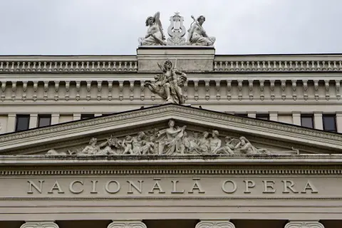 Elegancka fasada budynku opery w stylu neoklasycyzmu, ozdobiona rzeźbami i napisem "NACIONĀLĀ OPERA".