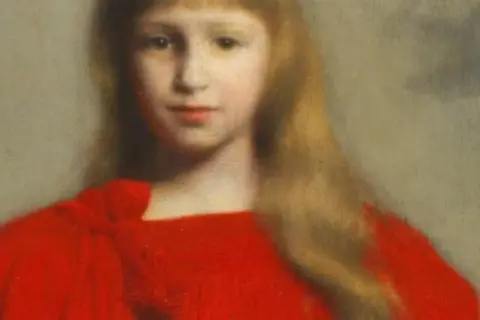 Portret dziewczynki w czerwonej sukience, z długimi blond włosami i łagodnym spojrzeniem.