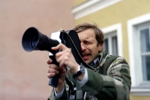 Jerzy Stuhr w filmie Kieślowskiego, z kamerą w ręku, skupiony na kadrze.
