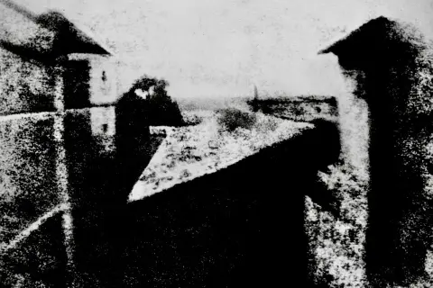Widok z okna, jeden z pierwszych fotografii. Dachy i budynki w szarościach.