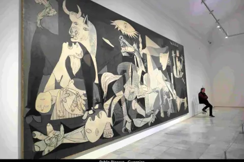 Pablo Picasso najsłynniejsze obrazy: "Guernica" w muzeum, z człowiekiem siedzącym na krześle i kontemplującym dzieło.