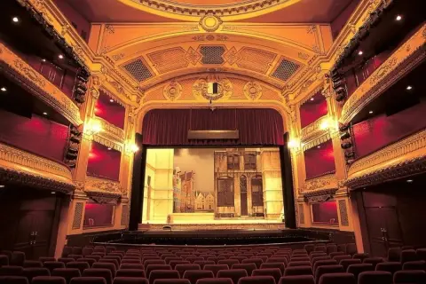 Widok na salę teatralną z rzędami czerwonych foteli i sceną z dekoracjami.
