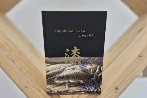 Okładka książki "Japońska laka urushi" z motywem złotej ryby koi i japońskiego znaku.