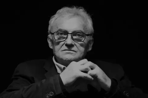 Portret Janusza Kondratiuka, reżysera znanych filmów, z dłońmi złożonymi na piersi.