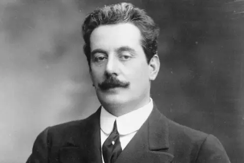Giacomo Puccini, kompozytor słynnych oper, w eleganckim garniturze. Jego muzyka wciąż porusza serca słuchaczy.