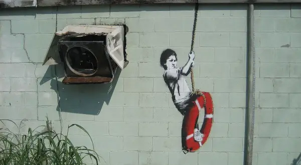 Dziecko na huśtawce z kołem ratunkowym, dzieło Banksy'ego. Kto to? Tajemniczy artysta uliczny.
