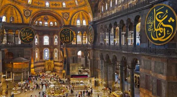 Wnętrze Hagia Sophia z widokiem na kopułę, kaligrafię i turystów. Plan budowli ukazuje jej monumentalność.