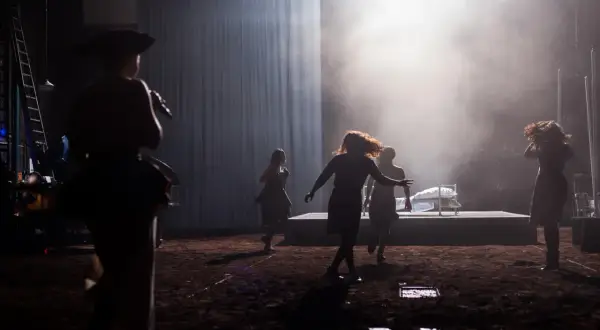Scena teatralna z kobietami w ruchu, w tle łóżko. Może to być scena z życia Johna Proctora.