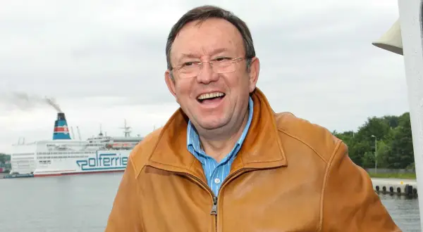 Uśmiechnięty Zbigniew Buczkowski w brązowej kurtce, na tle promu Polferries. Jego filmy, seriale i programy to klasyka polskiej rozrywki.