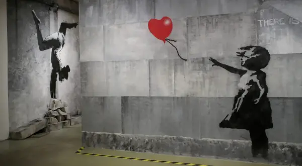 Dzieło Banksy'ego: dziewczynka sięga po czerwone serce, obok gimnastyczka na rękach. Kim jest Banksy? Tajemniczy artysta.