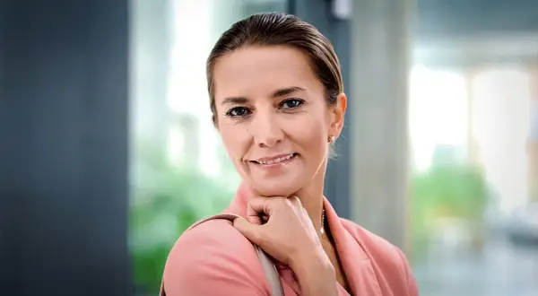 Uśmiechnięta Kamilla Baar, znana z filmów, seriali i programów, w różowej marynarce.