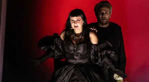 Dramatyczna scena z opery Karola Szymanowskiego. Kobieta w czarnej sukni i mężczyzna z wyrazem przerażenia na twarzy.