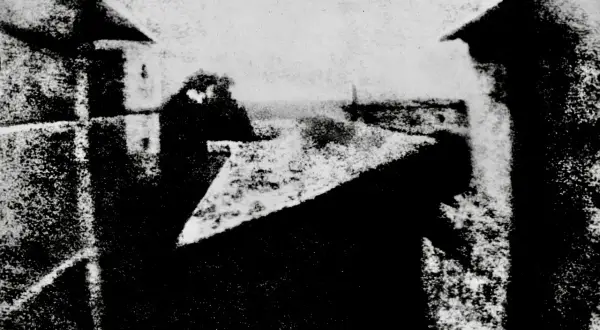 Widok z okna, jeden z pierwszych fotografii. Dachy i budynki w szarościach.