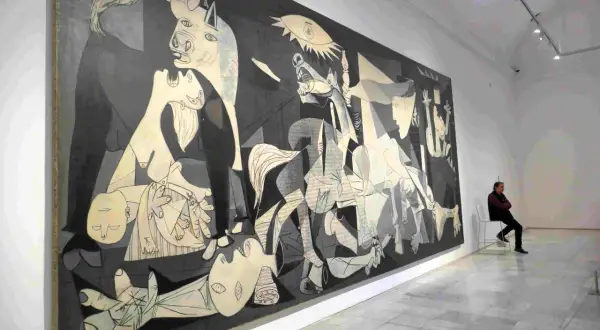 Pablo Picasso najsłynniejsze obrazy: "Guernica" w muzeum, z człowiekiem siedzącym na krześle i kontemplującym dzieło.