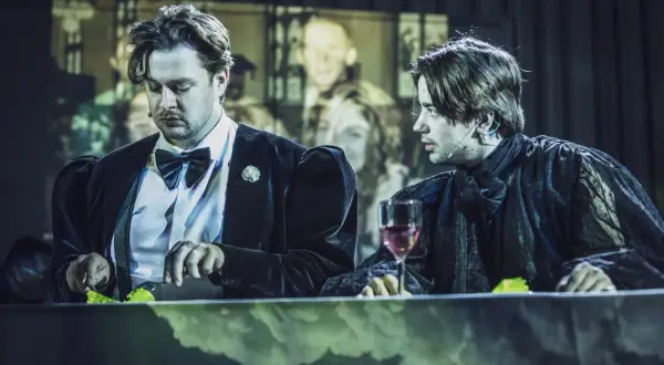 Dwóch mężczyzn przy stole, jeden w czarnym aksamicie, drugi w koronkowej szacie. Może to Hamlet i Ofelia?