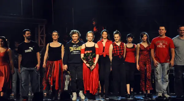 Aktorzy teatru buffo na scenie, w kolorowych strojach, pozdrawiają publiczność.