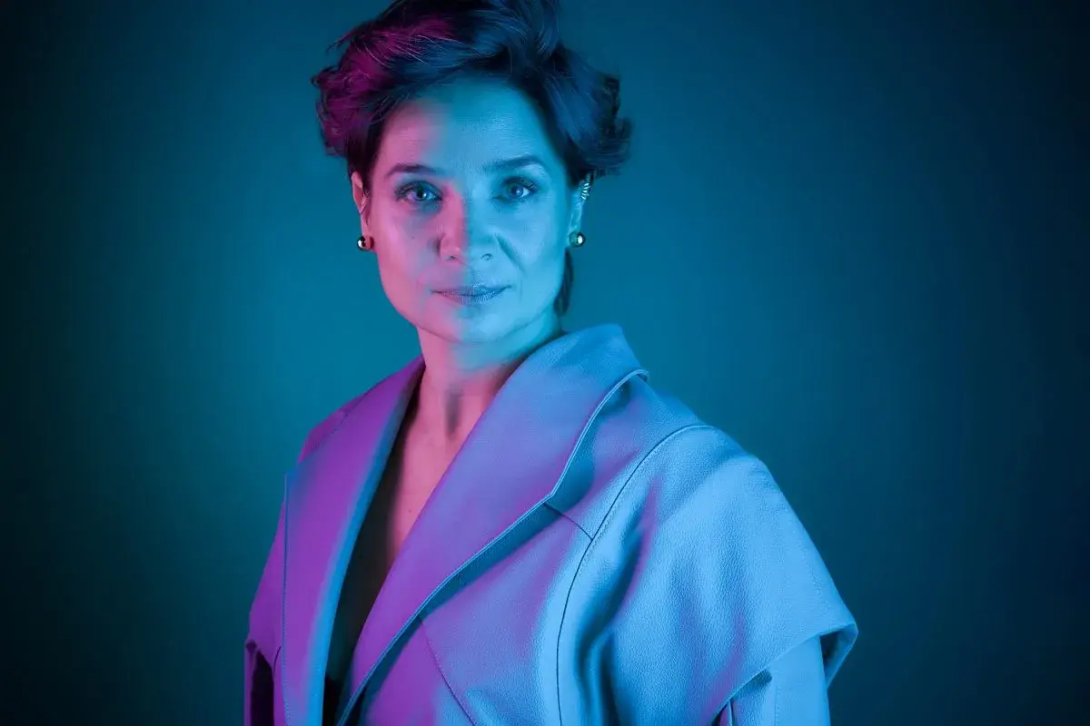 Barbara Sass, aktorka znana z filmów, w stylowej stylizacji, oświetlona neonowym światłem.