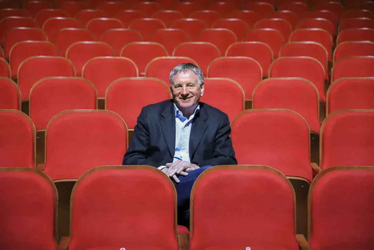 Uśmiechnięty dyrektor Teatru Osterwy siedzi wśród pustych, czerwonych foteli, gotów na kolejny spektakl.