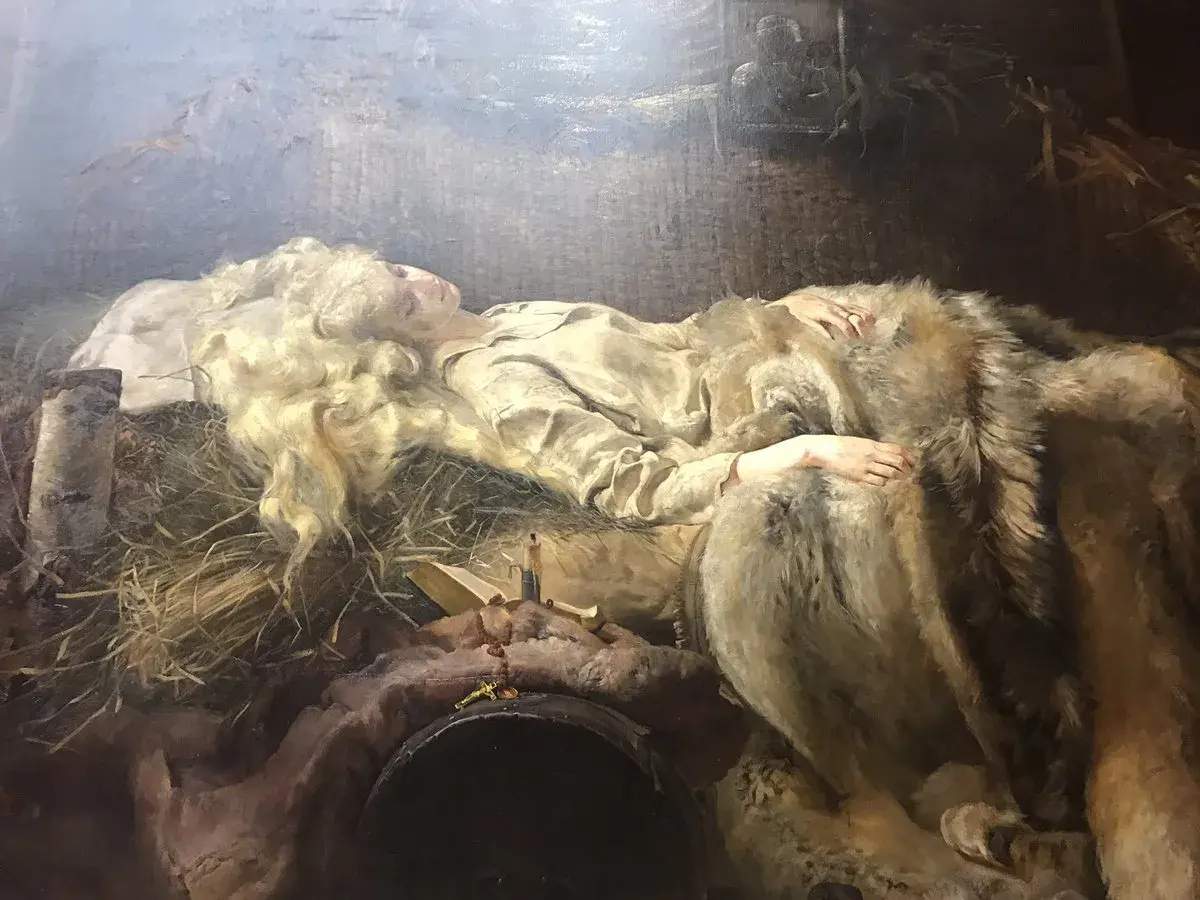 Młoda kobieta o blond włosach, Ellenai, śpi otulona futrem. Obok niej leży krzyż i książka.