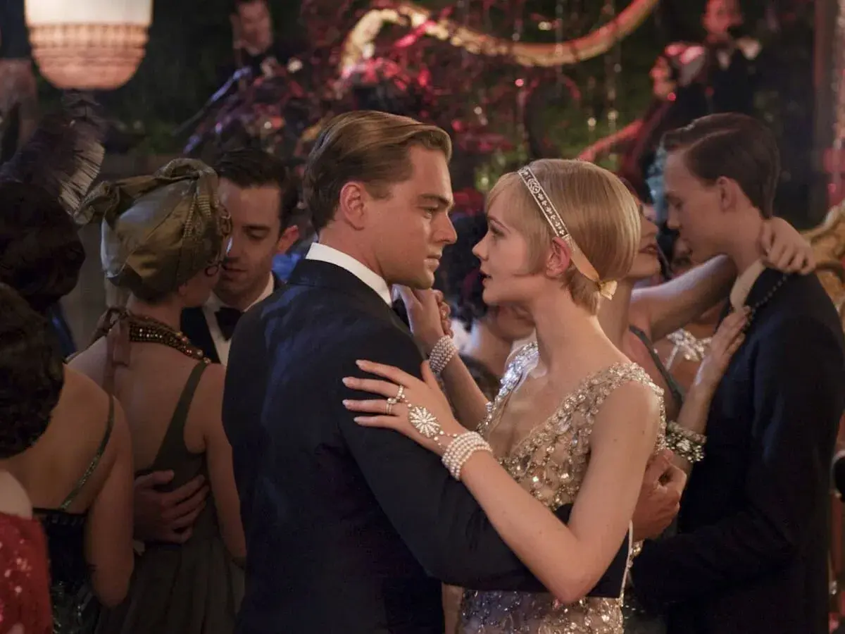 Para Gatsby'ego, taniec z Daisy to chwila magii. Ona w błyszczącej sukni, on w eleganckim garniturze, otoczeni gośćmi na przyjęciu.