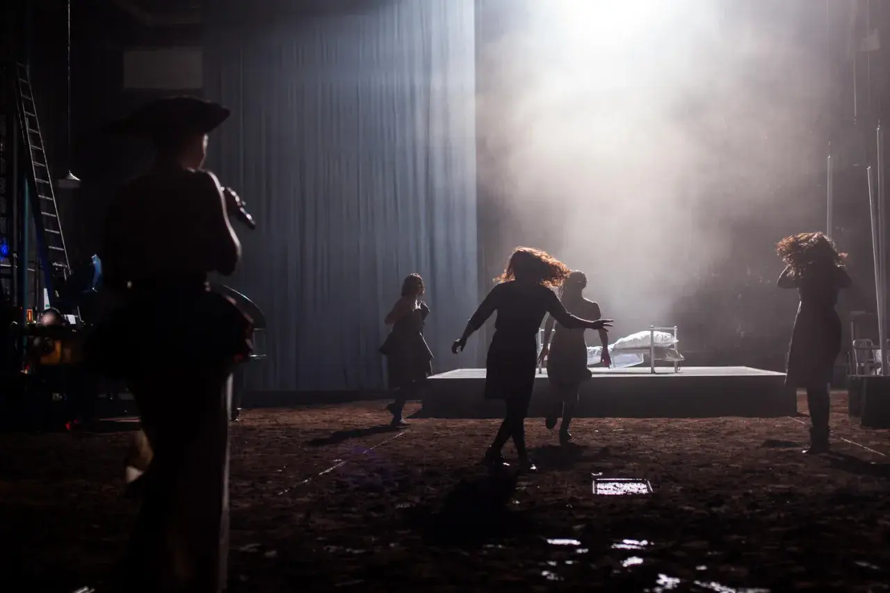 Scena teatralna z kobietami w ruchu, w tle łóżko. Może to być scena z życia Johna Proctora.