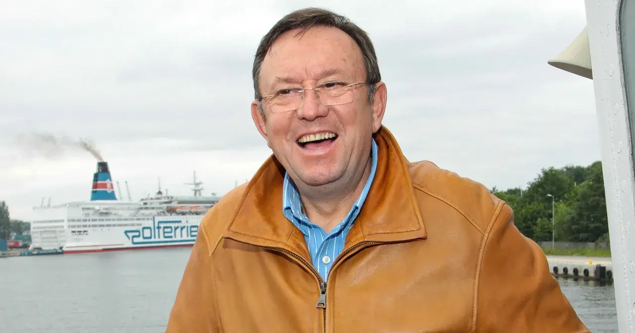 Uśmiechnięty Zbigniew Buczkowski w brązowej kurtce, na tle promu Polferries. Jego filmy, seriale i programy to klasyka polskiej rozrywki.