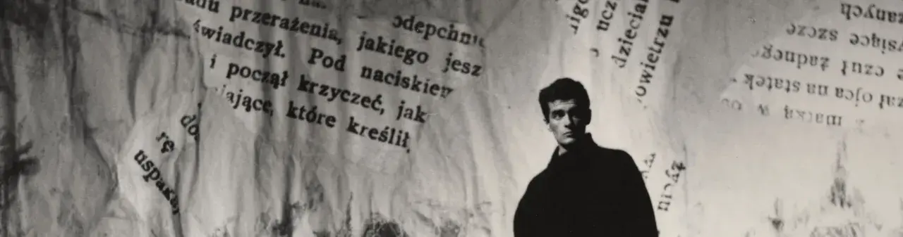 Młody mężczyzna, być może Hanuszkiewicz, stoi na tle podartych kartek z tekstem.
