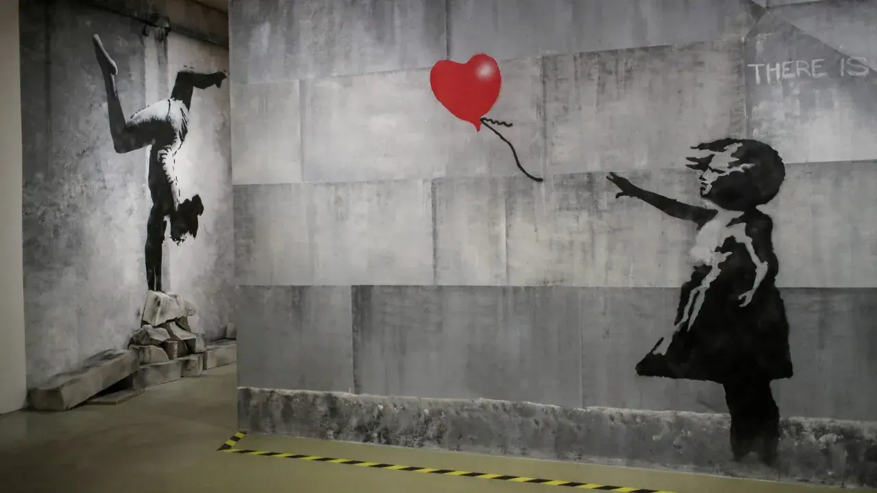 Dzieło Banksy'ego: dziewczynka sięga po czerwone serce, obok gimnastyczka na rękach. Kim jest Banksy? Tajemniczy artysta.