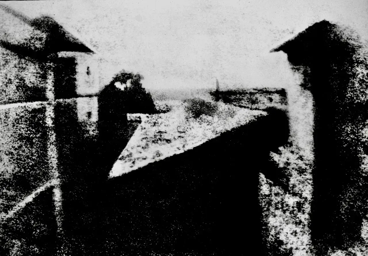 Widok z okna, jeden z pierwszych fotografii. Dachy i budynki w szarościach.