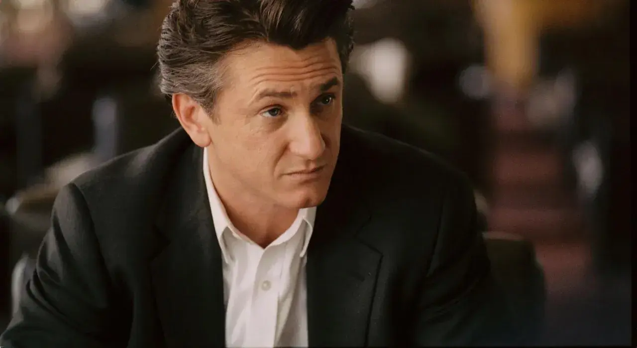 Sean Penn w czarnym garniturze i białej koszuli, zamyślony. Jego role w filmach zapadają w pamięć.