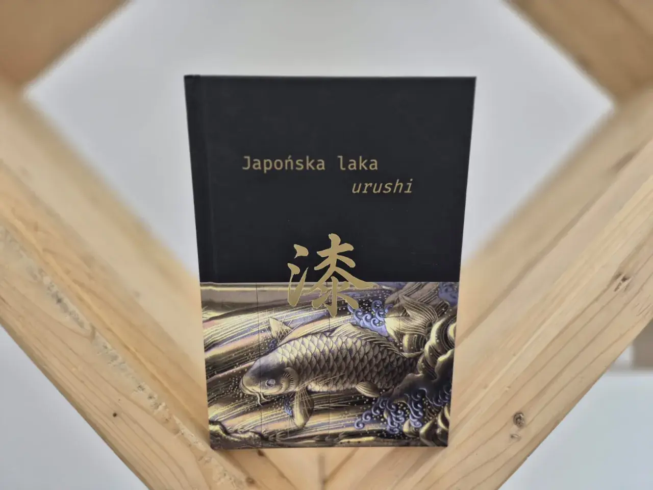 Okładka książki "Japońska laka urushi" z motywem złotej ryby koi i japońskiego znaku.