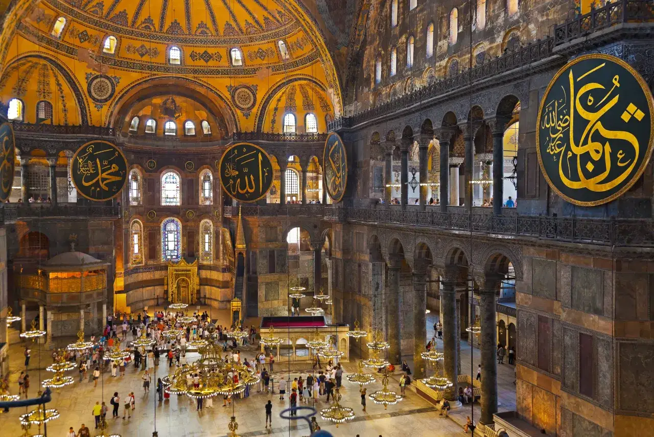 Wnętrze Hagia Sophia z widokiem na kopułę, kaligrafię i turystów. Plan budowli jest imponujący.