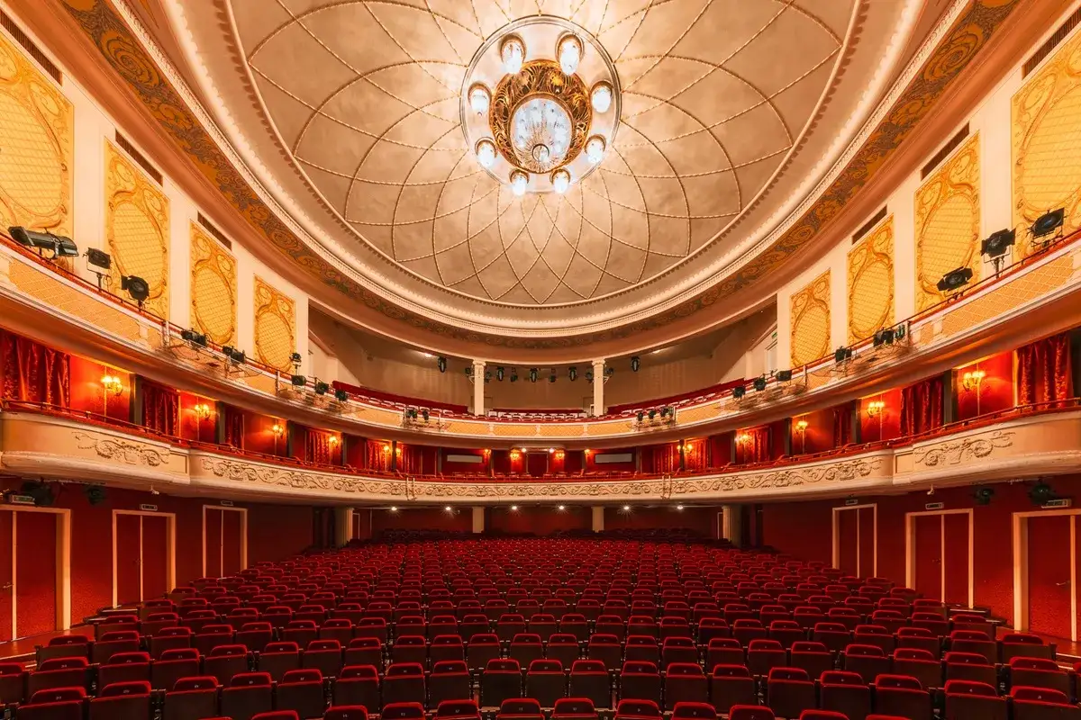 Wnętrze teatru z rzędami czerwonych foteli i bogato zdobionym sufitem. Czekamy na kolejne wspaniałe teatr spektakle!