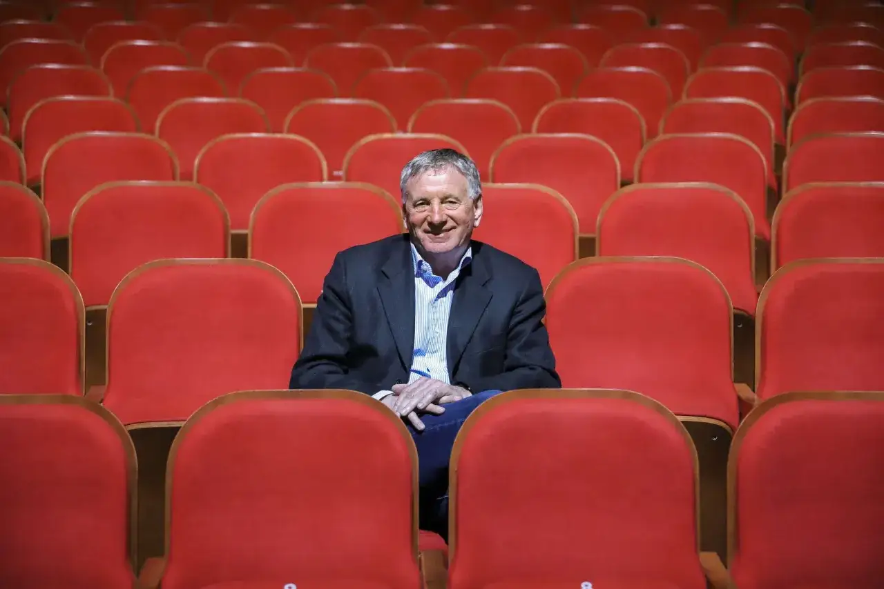 Uśmiechnięty dyrektor Teatru Osterwy siedzi wśród pustych, czerwonych foteli, gotów na rozpoczęcie spektaklu.
